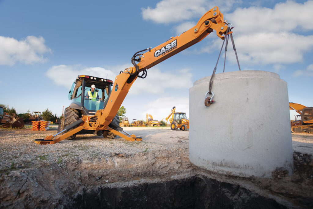 An operator performing safe lifting with excavators using a CASE excavator to lower a large concrete load into a trench on a construction site