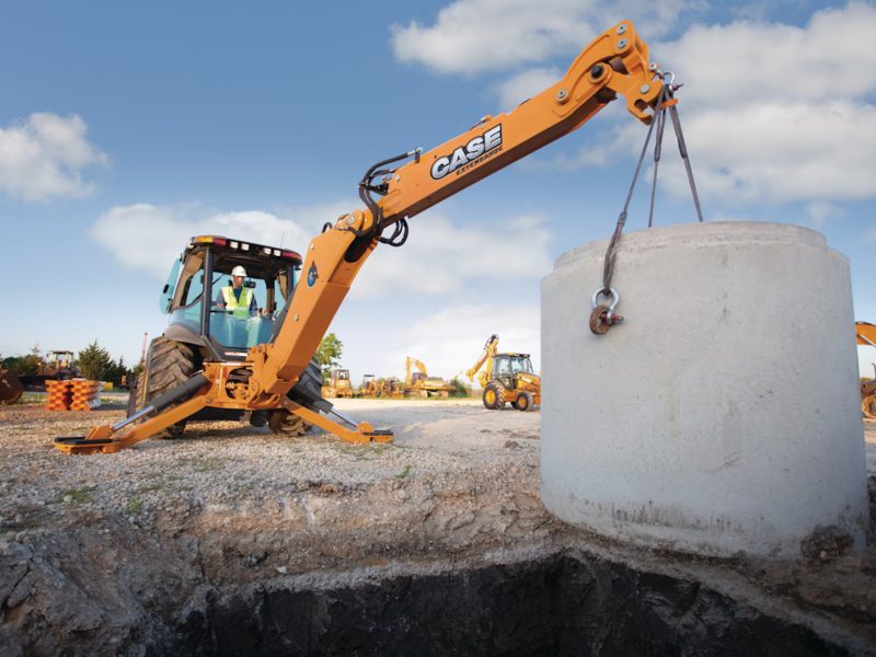 An operator performing safe lifting with excavators using a CASE excavator to lower a large concrete load into a trench on a construction site